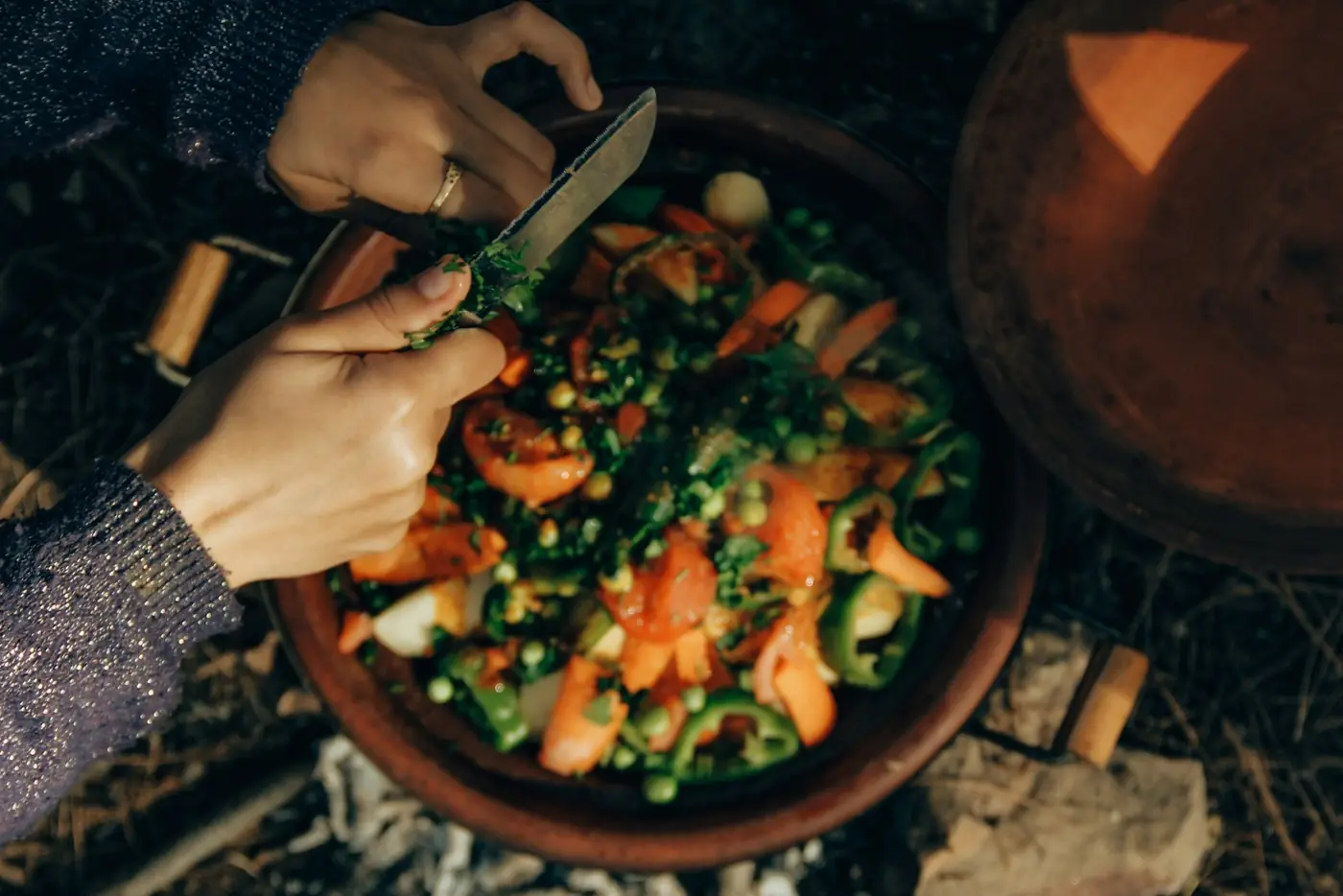 Hands slicing vegetables over a clay tagine